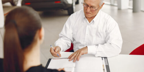 Old man in a car salon. Senior buying the car. Grandfather byu a car. Man talking with manager.